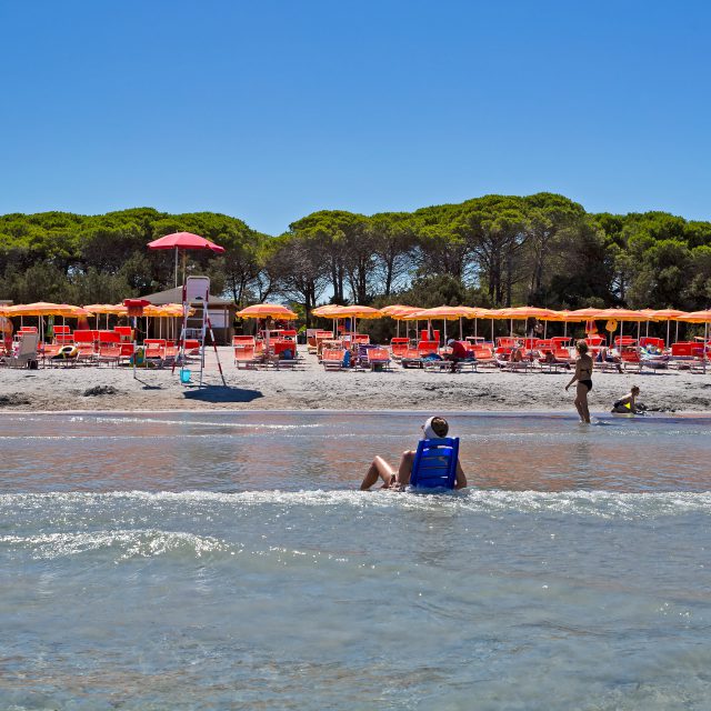 Tourist sitting in the middle of the sea, on Cala Ginepro beach in Sardinia